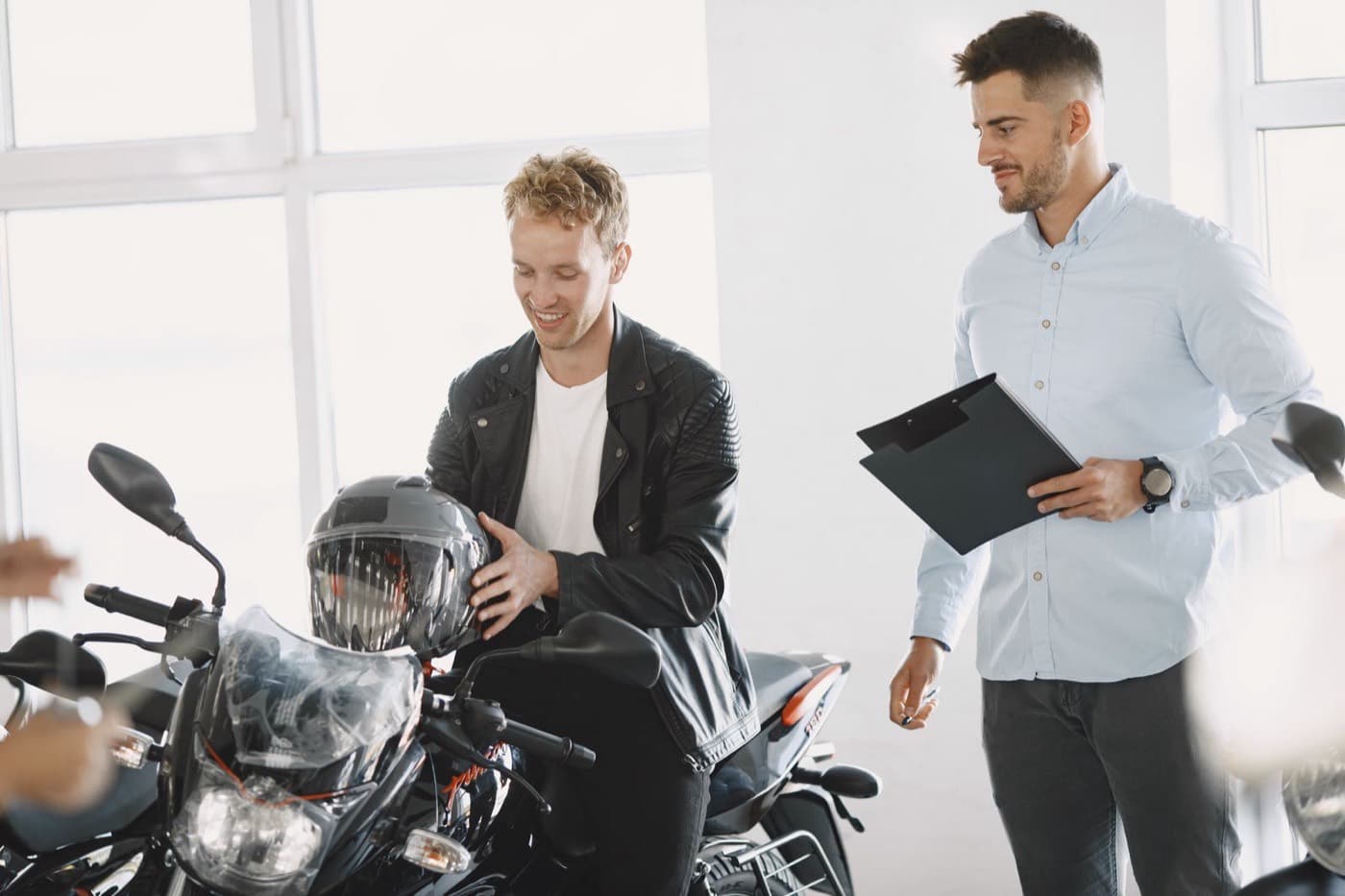 A dealership sales associate reviewing paperwork with a customer beside a motorcycle